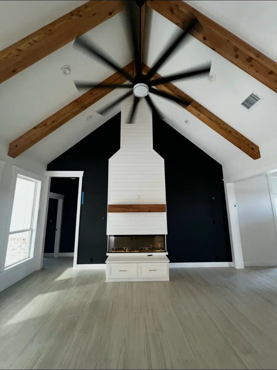 Custom home living room with vaulted ceiling, exposed wood beams, and a shiplap fireplace built by Elite Solutions of Texas