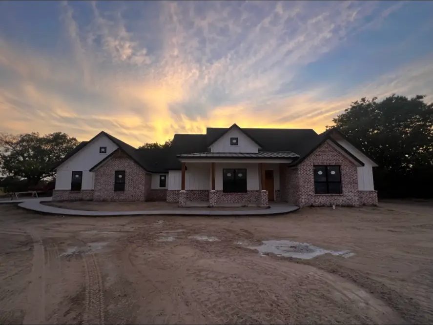 Completed barndominium-style home with board-and-batten siding and brick accents at sunset by Elite Solutions of Texas